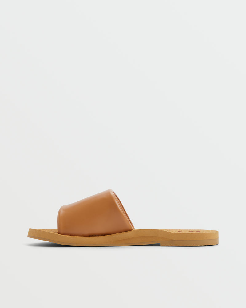 The Roxy Amalfi Coast Slide Sandal features a tan, smooth leather upper and a flat light brown sole. Displayed against a plain white background, this easy slide-on style offers comfort and versatility.