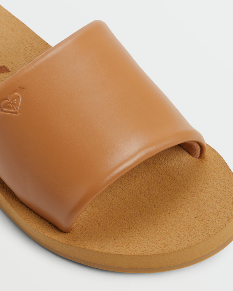 Close-up of the Roxy Amalfi Coast Slide Sandal, a tan sandal with a wide, smooth leather strap and textured footbed. Features an embossed heart-shaped logo on the side strap, shown against a white background.