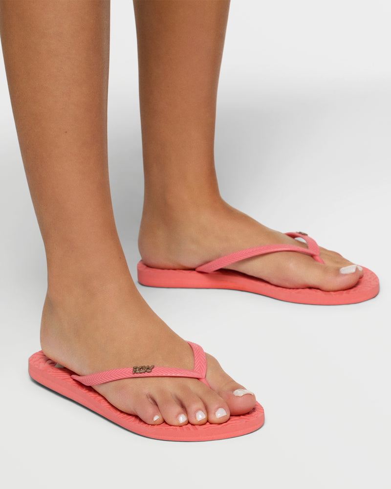 Close-up of a person wearing Roxy Antilles II Sandals in coral pink, featuring a textured sole and metallic logo on the straps, with neatly groomed toenails. Set against a plain white background.