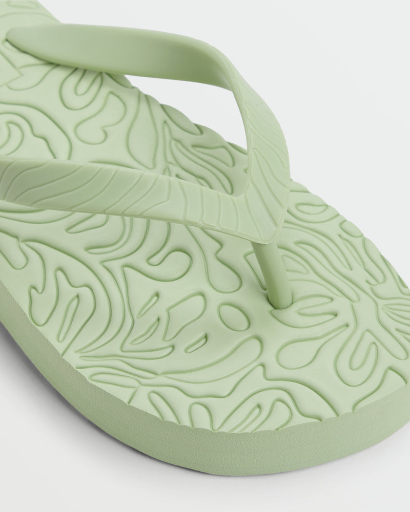 A close-up of a light green Roxy Beach Up Sandal shows its textured, wavy insole and matching thong strap. The photo highlights the detailed design and soft material, making this sandal ideal for casual beachwear.