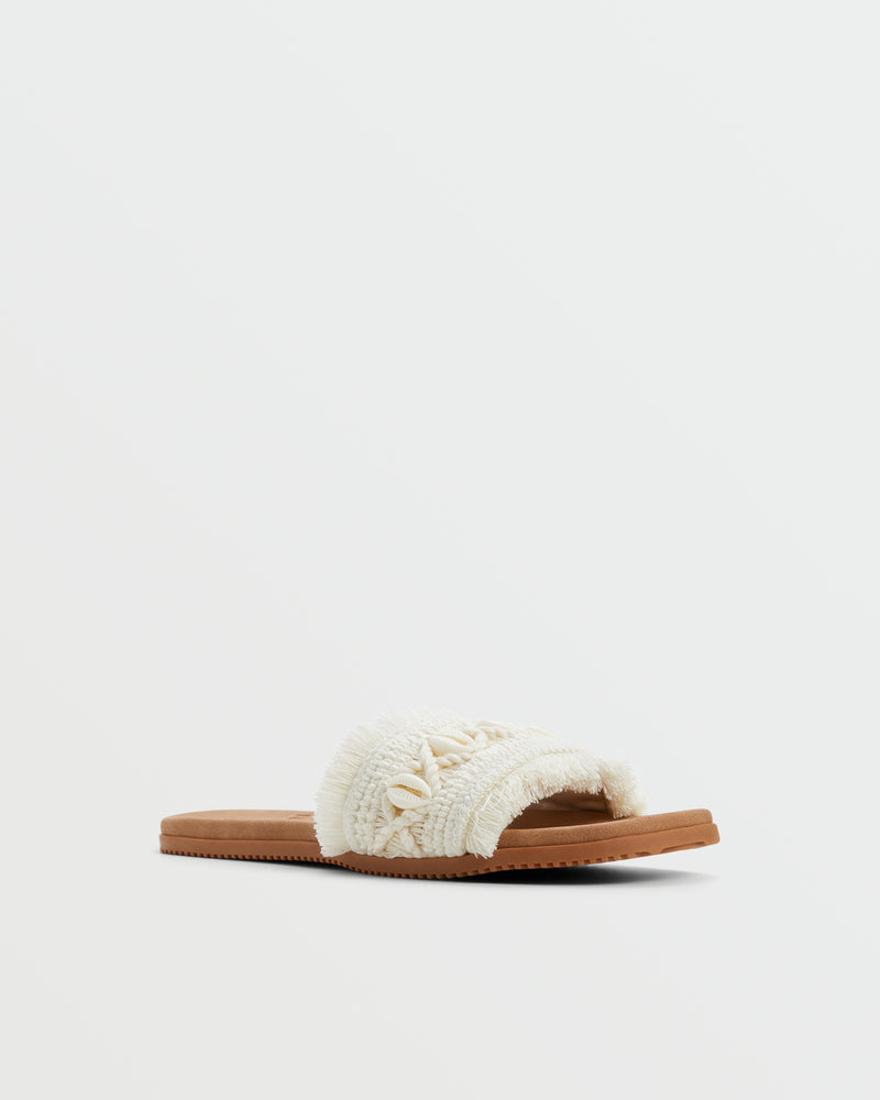 The Roxy Positano Sandal is a single beige slide with a textured, woven upper, small decorative shells, and a flat brown sole, shown on a plain white background.