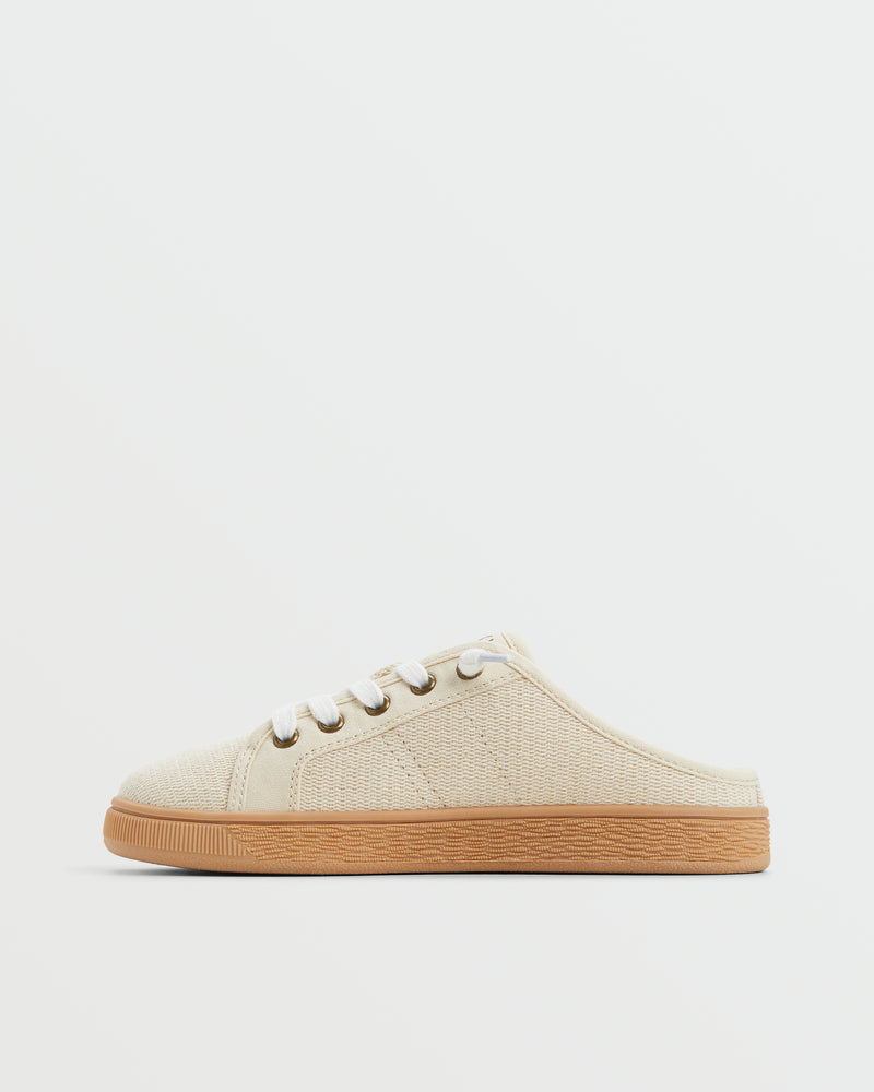The Roxy Sunny Stroll Mule Sneaker is a beige slip-on with a canvas upper, white laces, and a brown rubber sole, shown in profile against a plain white background.