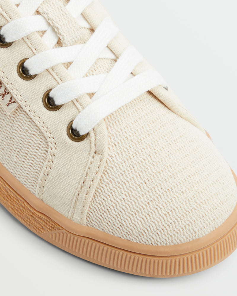 Close-up of the Roxy Sunny Stroll Mule Sneaker in beige canvas with white laces, metal eyelets, and a light brown rubber sole. The fabric texture and detailed stitching are clearly visible.