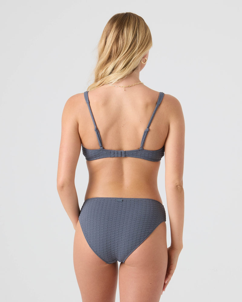 A woman with long blonde hair is shown from the back, wearing the Roxy Haleiwa Hipster Full Bikini Bottom in textured gray for ultimate comfort, set against a plain light background.