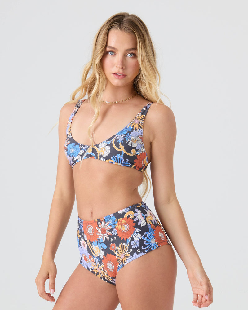 A woman with long, wavy blonde hair wears the Roxy Soul Flower Boyleg Bikini Bottom with a matching top, standing against a plain light background and looking at the camera with a neutral expression.