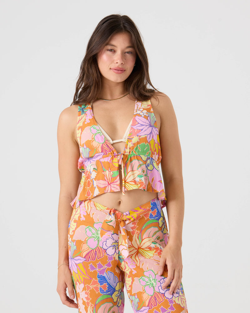 A woman with long brown hair wears the Roxy Lei It On Me Cover Up Pant, a high-waisted, Brown Multi floral print beachwear featuring pink, orange, purple, and green flowers. She stands against a plain light background.