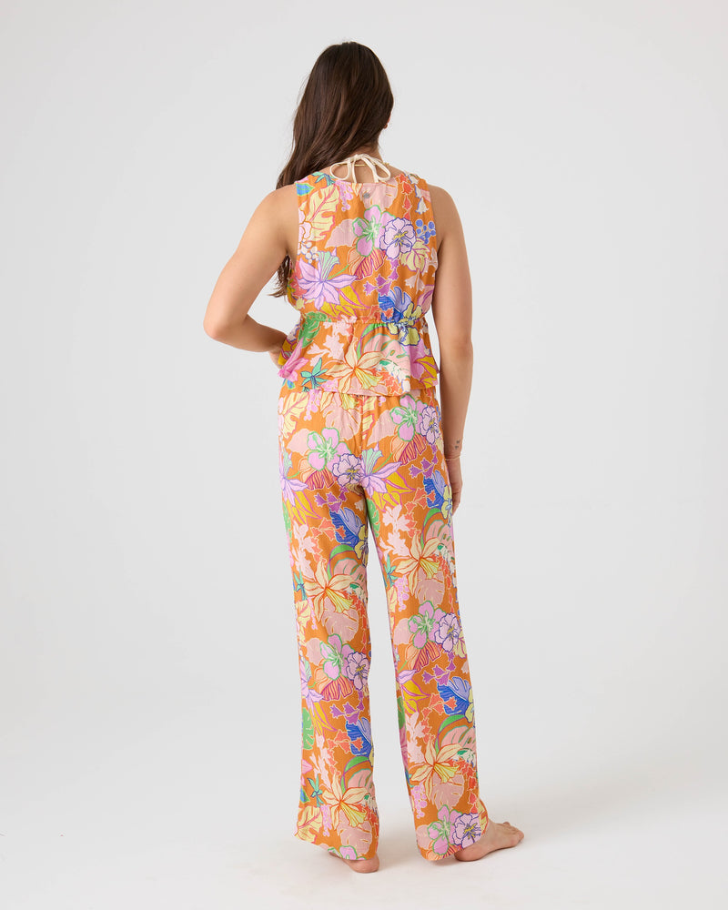 A person with long brown hair, seen from behind, wears the Roxy Lei It On Me Cover Up Pant in bright Brown Multi floral print and a matching sleeveless halter-neck top—perfect beachwear—standing barefoot on a white backdrop.