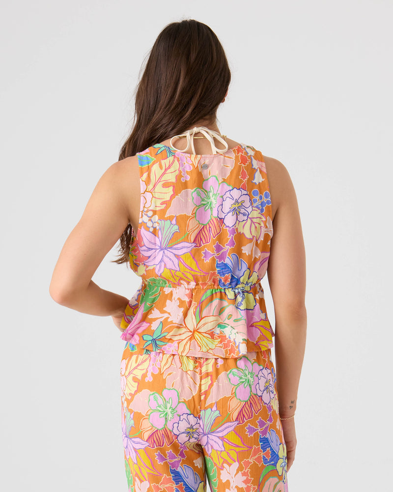A woman with long brown hair faces away, wearing the Roxy Lei It On Me Cover Up Top—a sleeveless top with a tie-neck and gathered waist, featuring a vibrant floral pattern in pink, orange, green, blue, and purple. Perfect for chic beachwear.