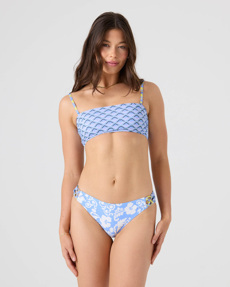 A woman with long brown hair stands against a plain background, wearing the Roxy Golden Glow Lace Up Bandeau Bikini Top in light blue with a floral pattern, made from recycled nylon. She faces forward and smiles slightly, enhancing her look.