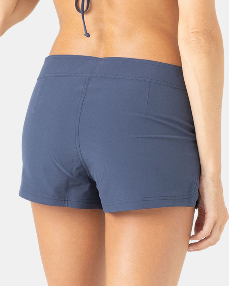 A person is shown from the waist down and back view, wearing Roxy To Dye 2" Boardshorts and a bikini top, against a light gray background.