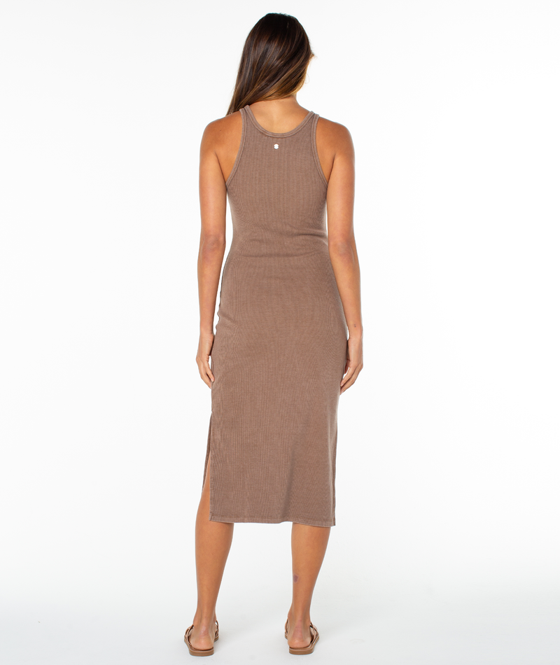 A woman stands with her back to the camera, wearing the Roxy Emilia Midi Dress—a sleeveless, ribbed, high neck cotton blend dress—paired with sandals against a plain white background.