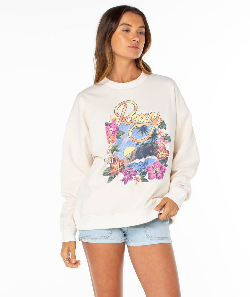 A woman models the Roxy Lineup Oversized Crew sweatshirt, featuring a colorful floral and palm tree graphic, paired with light denim shorts, standing against a plain white background.