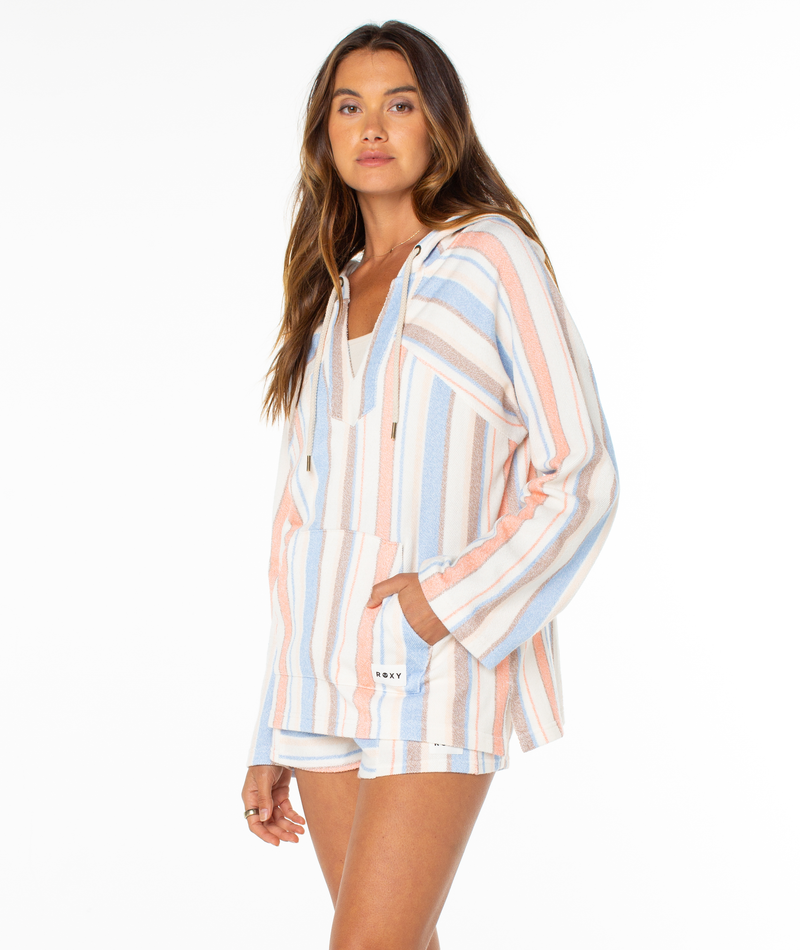 A woman wears the Roxy Wild And Free Hoodie, a relaxed-fit, hooded long-sleeve top with summery blue, pink, and white stripes, paired with matching shorts against a plain white background.