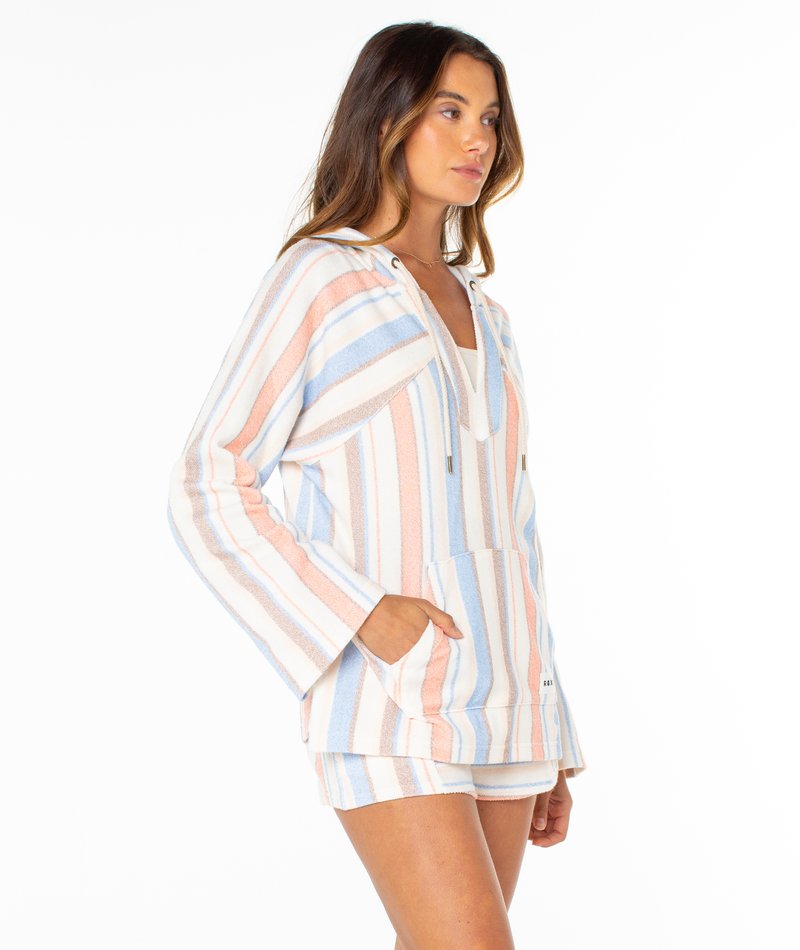 A woman models the Roxy Wild And Free Hoodie, a relaxed fit pullover with summery pastel blue, peach, and white stripes, paired with matching shorts. She stands at an angle against a plain white background.