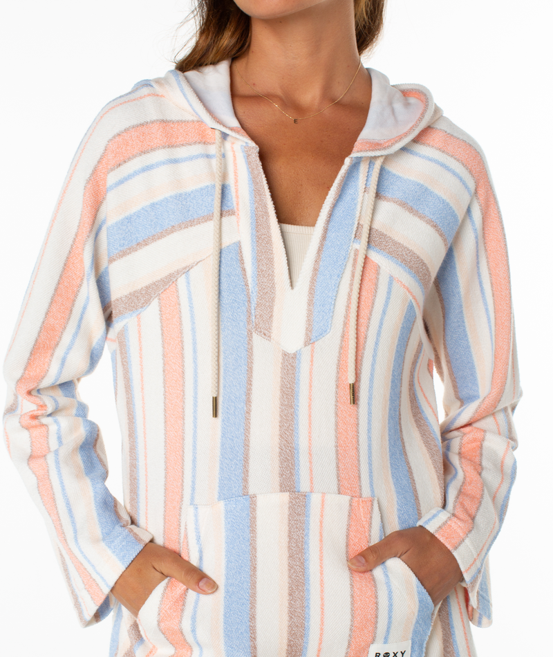 A woman in the Roxy Wild And Free Hoodie—a cozy, relaxed-fit top with pastel blue, peach, and white stripes, long sleeves, hood with drawstrings, and front pocket—captures effortless coastal style.