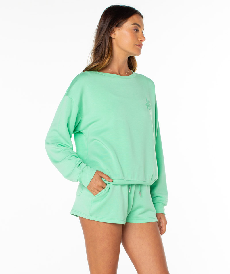 A woman stands in a relaxed pose with her left hand in her pocket, wearing a light green Roxy Surfing By Moonlight Top and matching shorts against a plain white background.