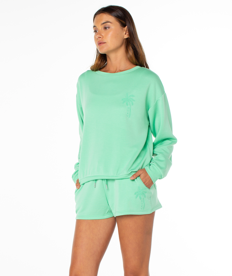 A woman models the Roxy Surfing By Moonlight Top in mint green with matching palm tree shorts, hands in pockets, against a plain white background.