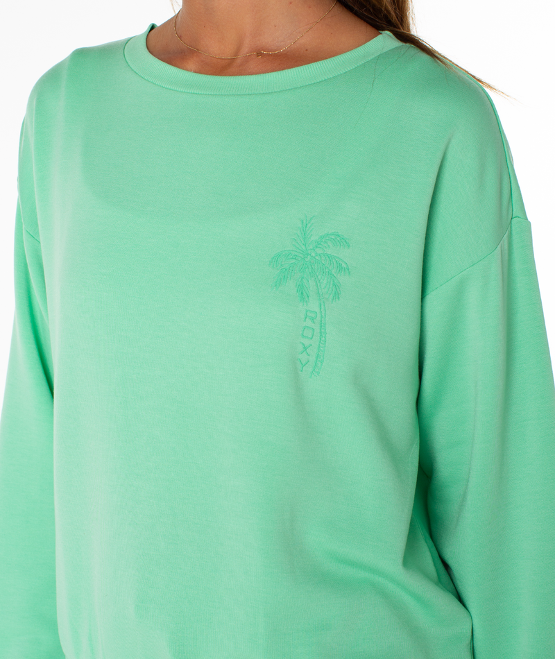 A person wearing the Roxy Surfing By Moonlight Top in light green, featuring a small palm tree and ROXY logo on the left chest. The image is cropped to show only their upper torso.