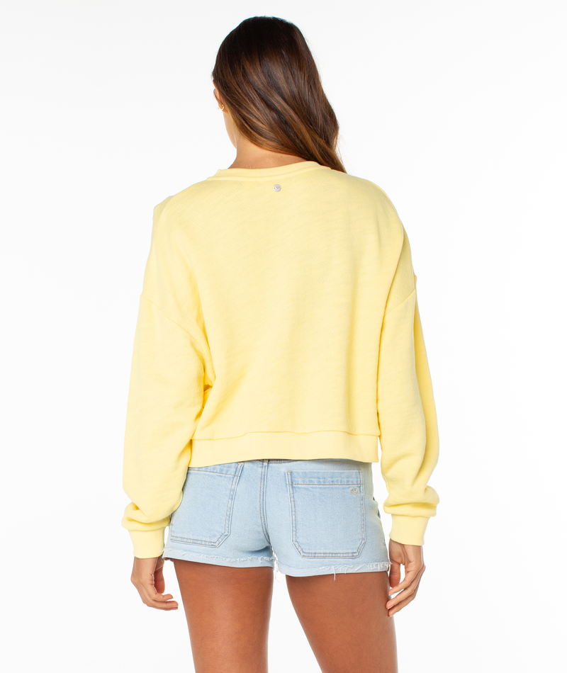 A woman stands with her back to the camera, wearing a light yellow Roxy Overcast Hoodie and light blue denim shorts against a plain white background.