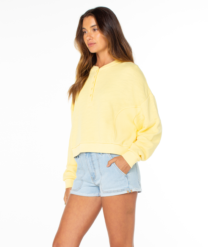 A woman with long brown hair and a neutral expression poses against a plain white background, wearing the Roxy Overcast Hoodie and light blue denim shorts.