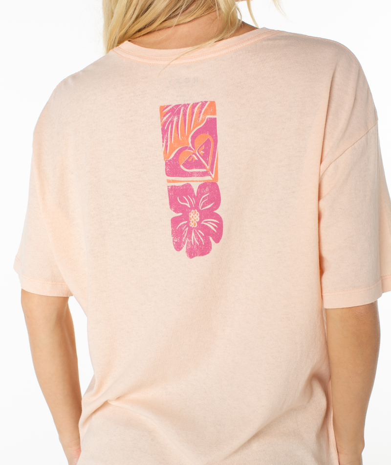 A person is seen from behind wearing the Roxy Beach Things Tee, an oversized light pink shirt with a vertical graphic of a pink and orange heart, leaves, and flower on the back. The relaxed drop-shoulder fit adds to its laid-back vibe.