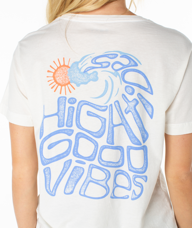 A person wears the Roxy High Tides Tee, a slouchy top with a vibrant back graphic of a blue wave, orange sun, and bold blue “HIGH GOOD VIBES” text.