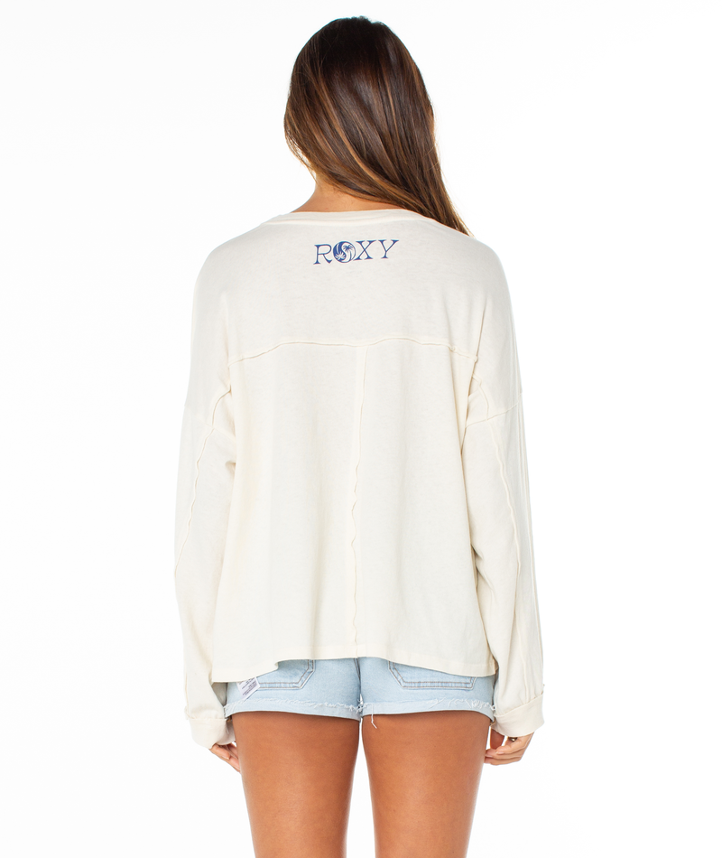 A woman with long brown hair, wearing the cream-colored Roxy Changing Tides Top with balloon sleeves and light denim shorts, stands facing away against a white background.