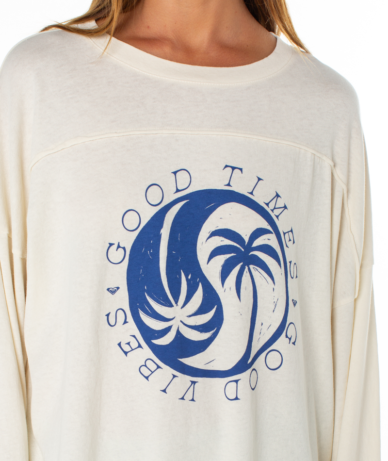 A woman wears the Roxy Changing Tides Top—an oversized cream sweatshirt with balloon sleeves, featuring a blue circular palm tree graphic and "GOOD VIBES GOOD TIMES" text.