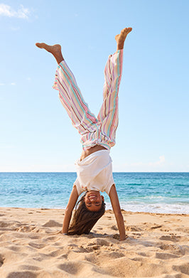 Person doing a handstand on a beach with clear blue sky and ocean.