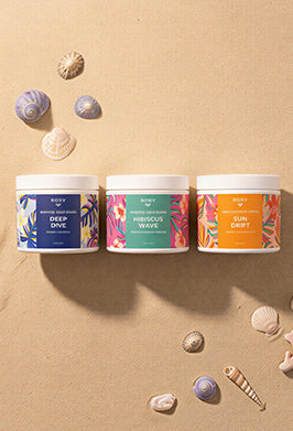 Three cylindrical containers with colorful labels on a sandy background with shells.