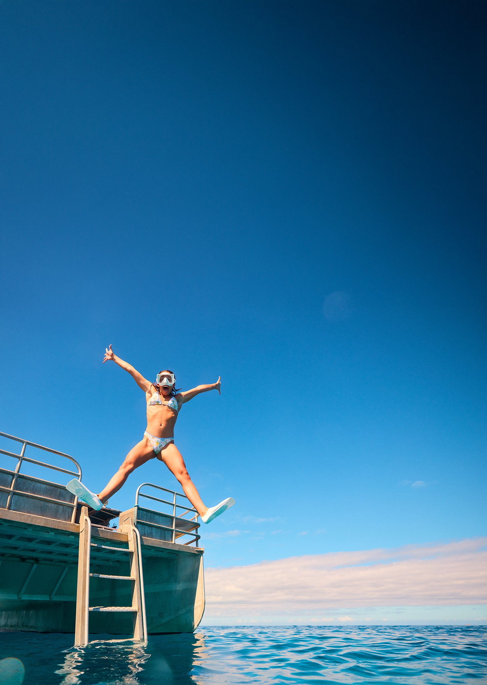 Person jumping off a dock into the water with a clear blue sky.