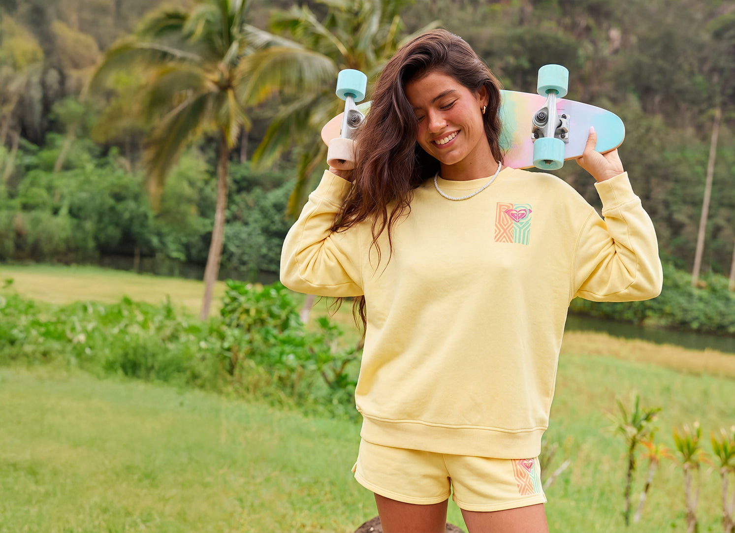 Person holding a colorful skateboard outdoors with greenery in the background