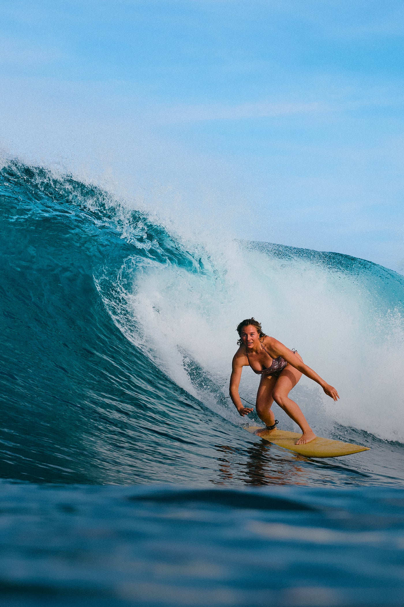 Person surfing on a wave in the ocean with clear blue sky.