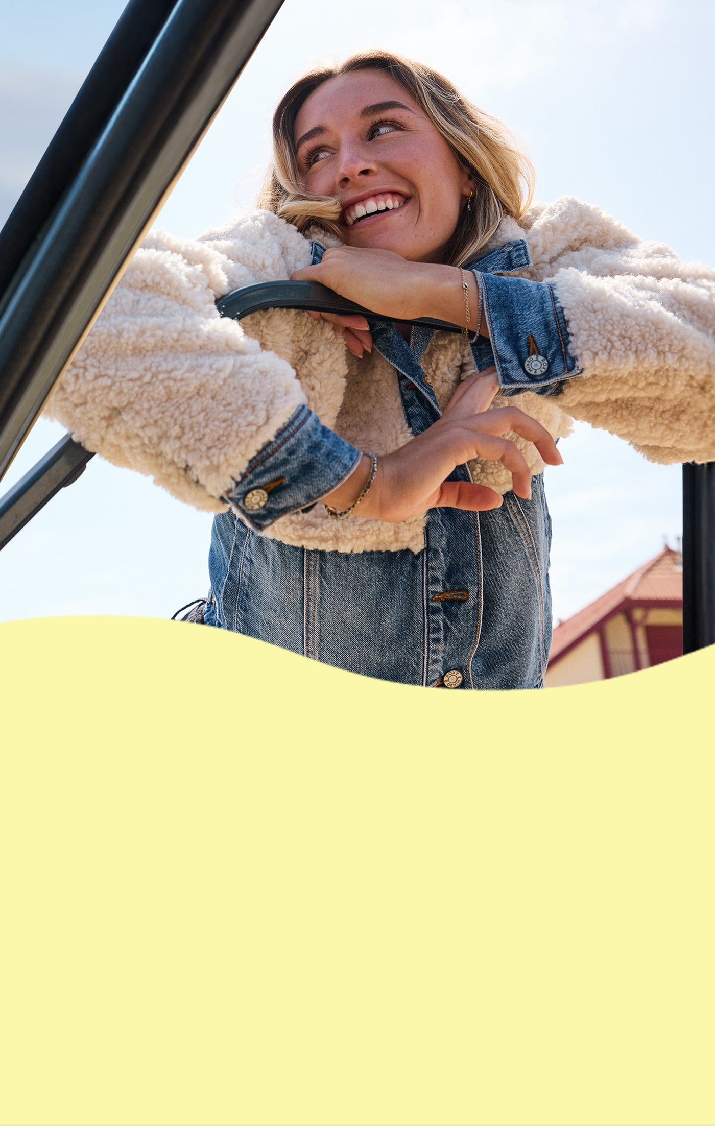 Woman in a beige coat and denim jacket standing next to a car with a clear sky background