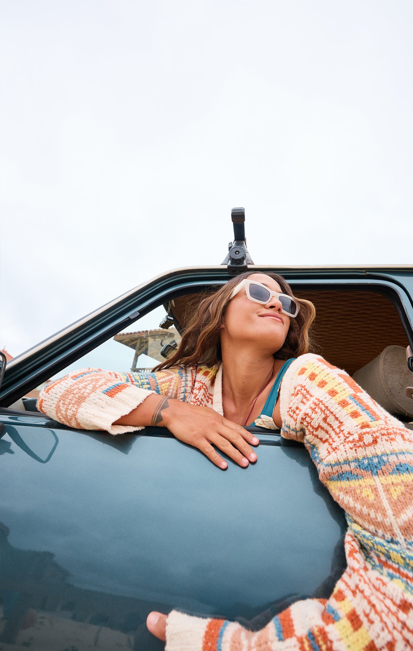 women wearing a colorful sweater and sunglasses looking out her car window