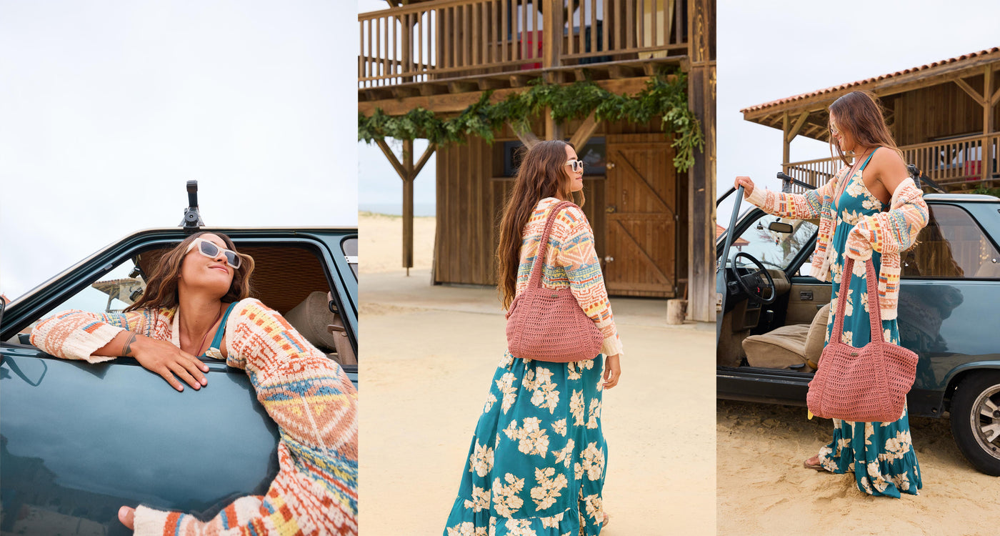 Woman in a colorful outfit with a floral skirt and pink bag near a car, with a wooden structure and people in the background.