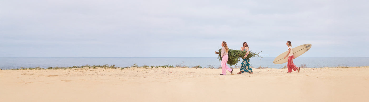 Three people walking on a sandy beach with surfboards.