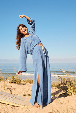 Woman in a blue outfit standing on a beach with clear blue sky