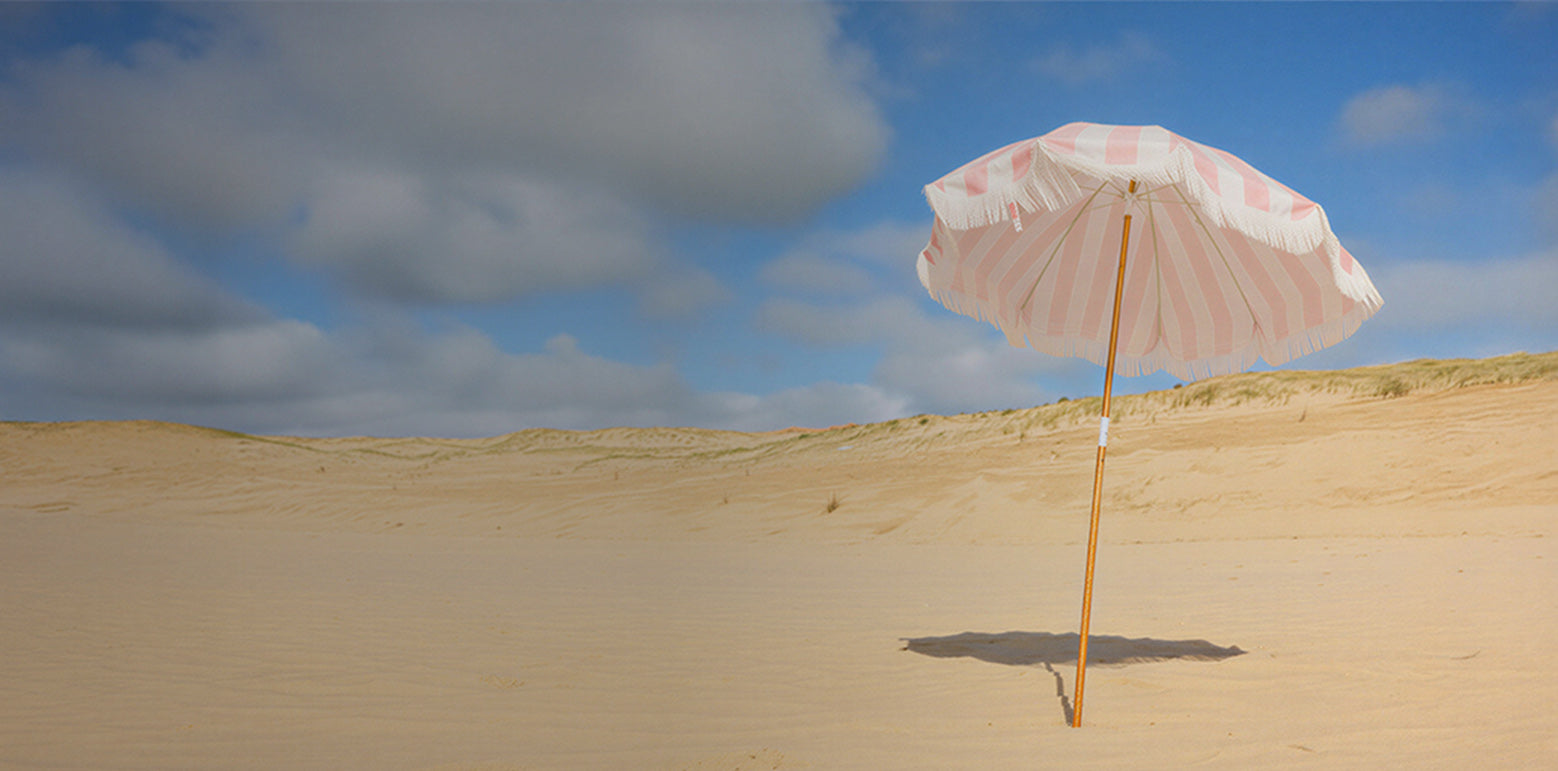 Pink beach umbrella with white pattern on a sandy dune under a blue sky with clouds