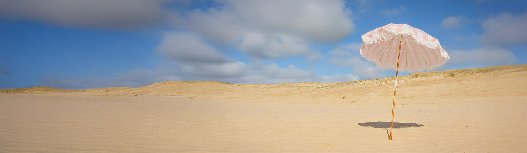 Pink beach umbrella on sand dunes with blue sky and clouds