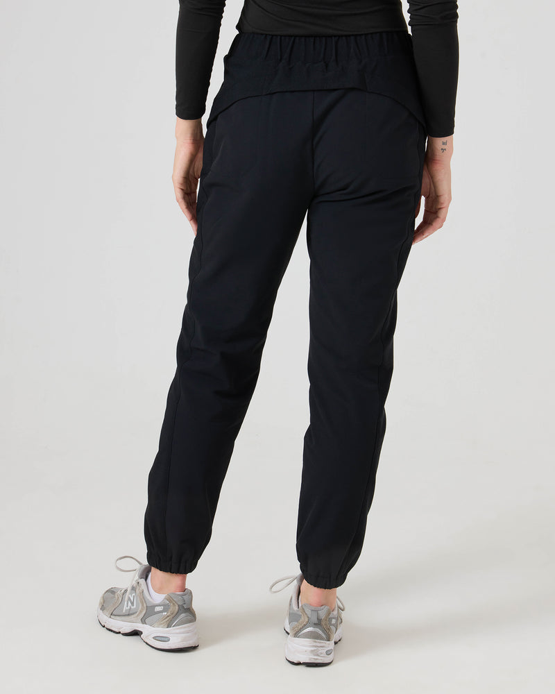 A person is shown from the back against a plain white background, wearing the Roxy Ember Textured Jogger in black, paired with a black long-sleeve top and gray sneakers.