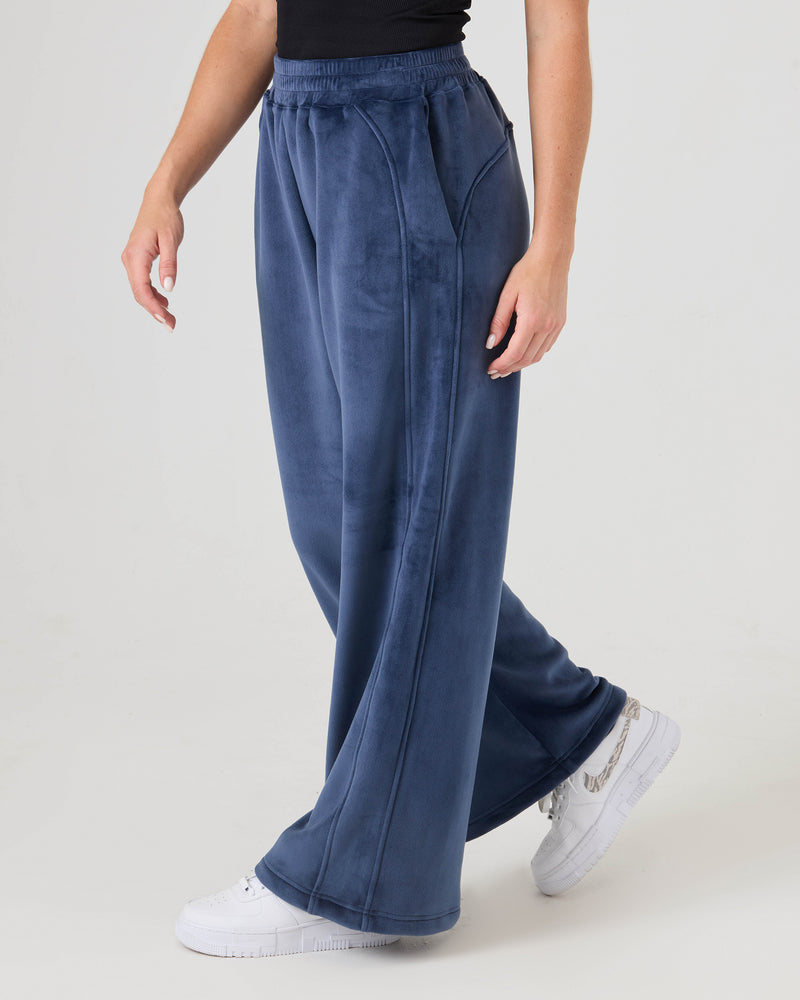 A person wears Roxy Vivi Bonded Velour Pants with a black sleeveless top and white sneakers, standing against a plain light background.