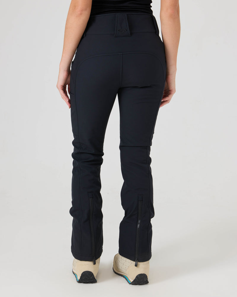 A person is shown from the back against a plain white background wearing the Roxy Haylee Softshell Pants—black fitted flare pants with back seams—paired with beige shoes and a black top.