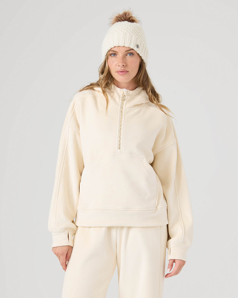 A woman stands facing the camera in a Roxy Vivi Bonded Pullover (Whitecap), matching sweatpants, and a white knit beanie with a brown pom-pom, against a plain light background.