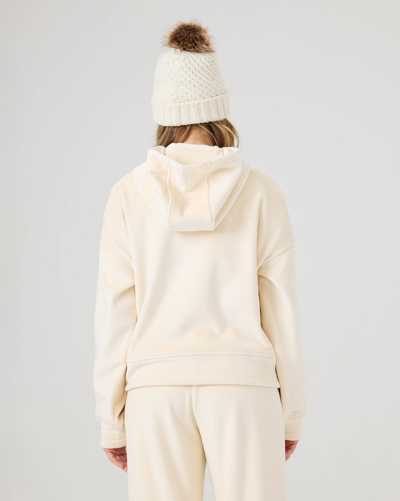 Person facing away, wearing the Roxy Vivi Bonded Pullover in cream and matching sweatpants, styled with a knit beanie topped by a brown pom-pom, against a plain light background.
