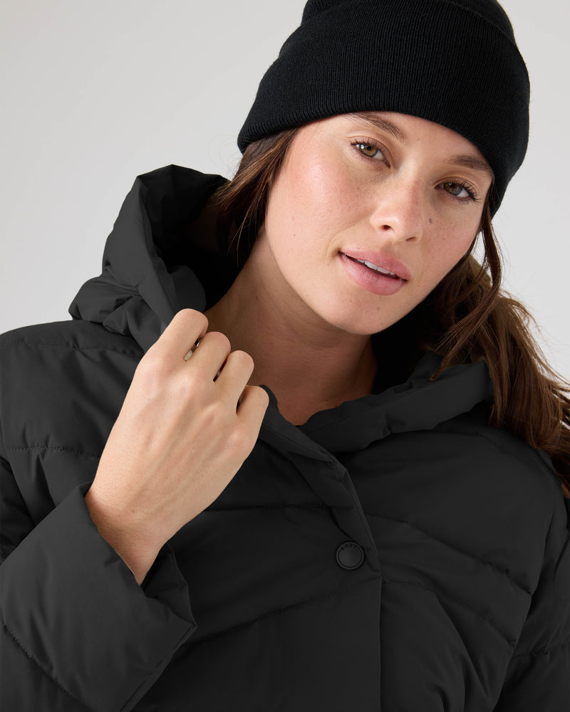 A person in the Roxy Abby Quilted Puffer and a black beanie looks at the camera, gently holding the jacket’s collar with one hand.