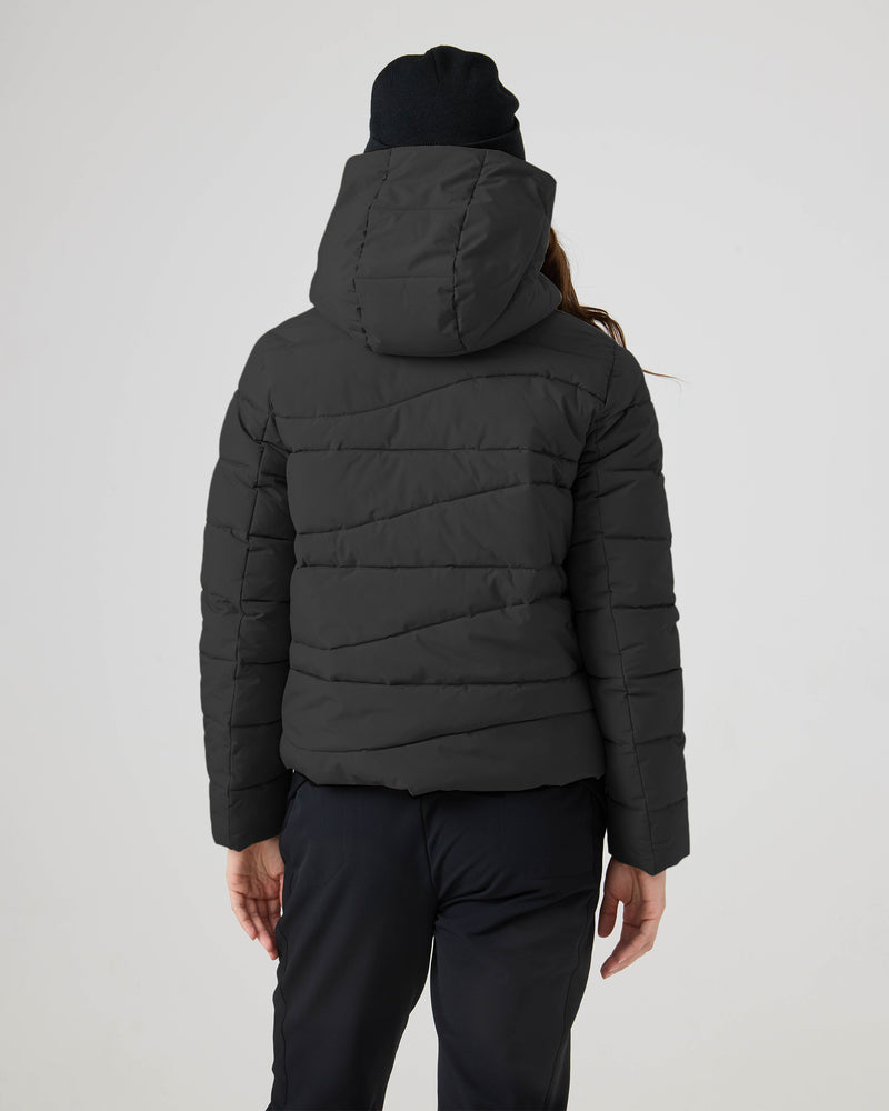 A person in the Roxy Abby Quilted Puffer, black pants, and a black beanie stands facing away, highlighting the jacket’s regular fit and hood—ideal for cool-weather style against a plain light background.