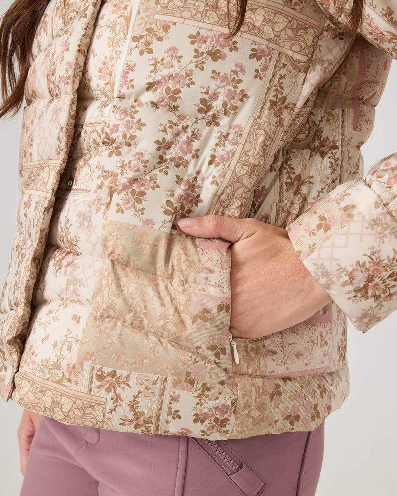 A close-up of a person wearing the Roxy Abby Quilted Puffer in a regular fit, with one hand in the pocket, paired with pinkish-purple pants featuring a zippered pocket. Only the lower torso and part of an arm are visible.