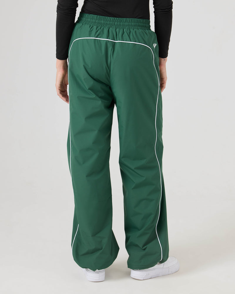 Model wears loose green Stevie Parachute Pants by Roxy with white piping and white sneakers, standing against a plain background, facing away from the camera.