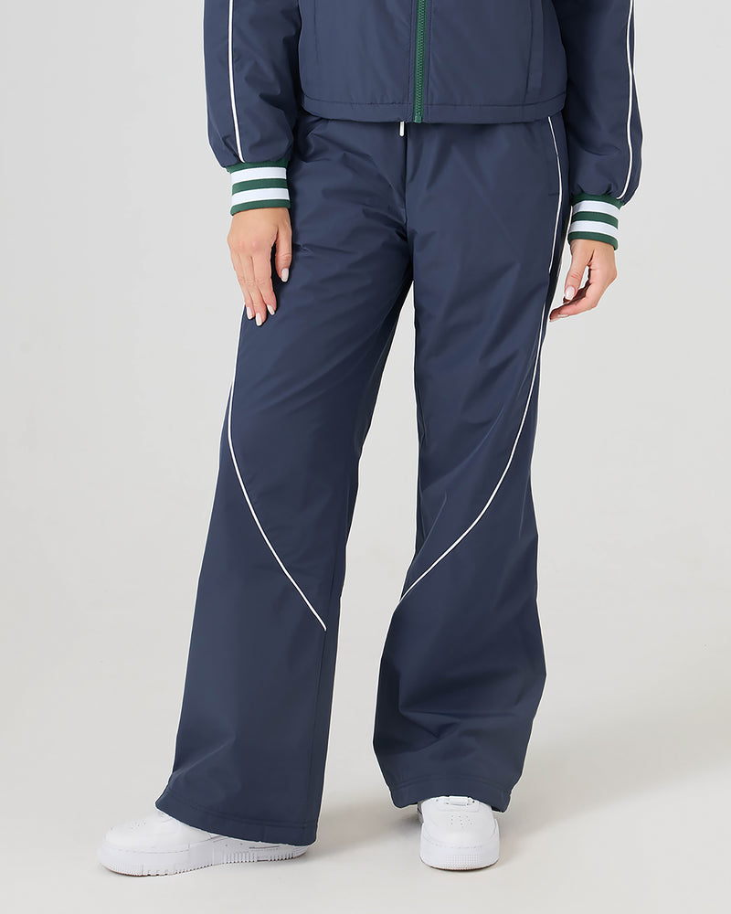 Model wears Roxy Stevie Parachute Pants—navy wide-leg pants with white piping and an adjustable waistband—paired with white sneakers, shown from the waist down against a plain background.
